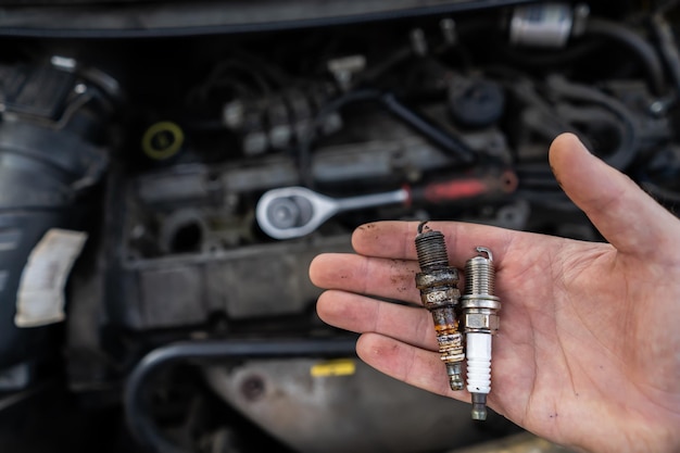 Vecchia e nuova candela nelle mani di un meccanico sullo sfondo del motore di un'auto