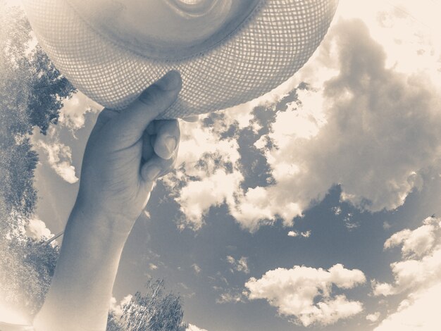 Vecchia foto d'epoca. Un uomo di razza caucasica tiene in mano un cappello. Sullo sfondo del cielo e delle nuvole bianche. Concetto astratto di vacanza estiva. Vista dal basso.