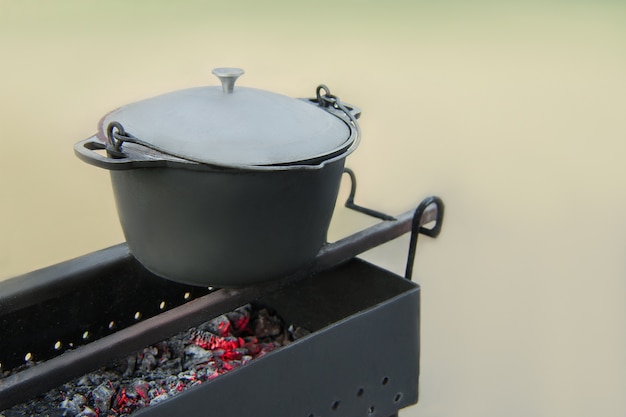 Vecchia padella in ghisa con fuliggine sulla griglia con carboni ardenti. Cucinare in una natura