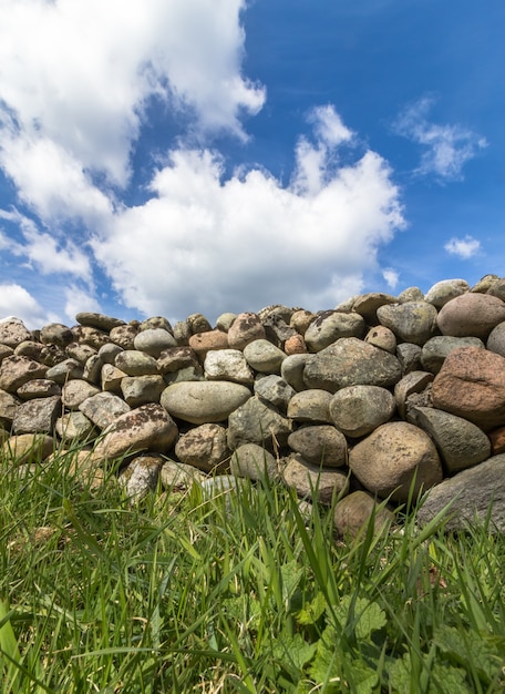 Vecchia parete di pietra con erba verde nella parte anteriore e cielo blu con le nuvole qui sopra, immagine verticale