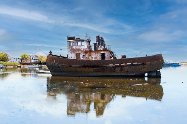 vecchia piccola nave arrugginita che galleggia in un fiume sotto il cielo blu