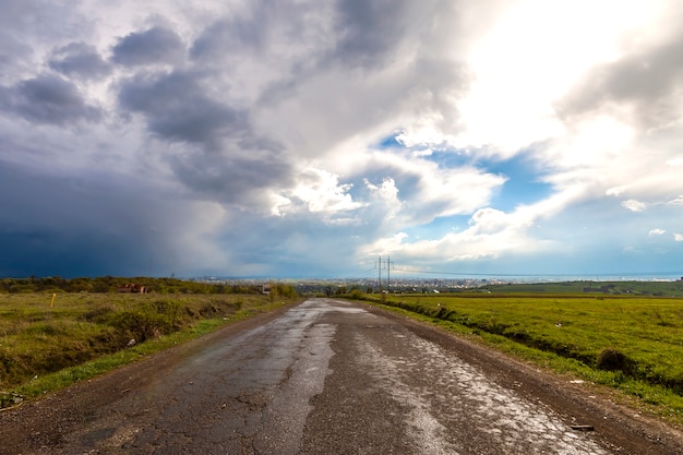 Vecchia strada incrinata dopo la pioggia. Cattiva strada accidentata con buchi e cielo nuvoloso tempestoso.