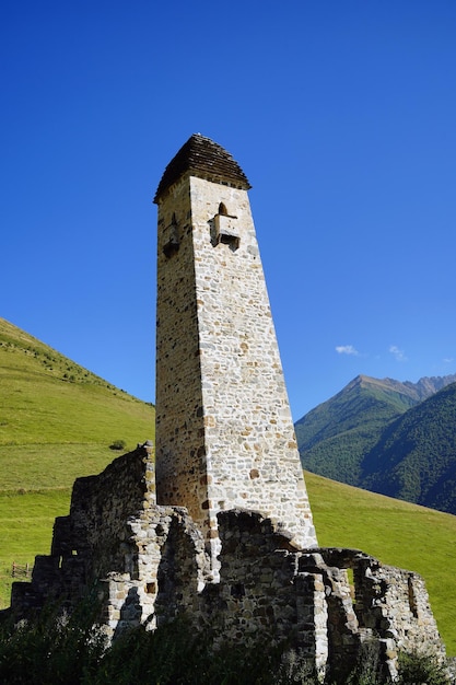 Vecchia torre di pietra nel verde terreno montuoso Antico edificio in pietra della città vecchia situato su una collina verde contro montagne coperte di foresta in un giorno d'estate