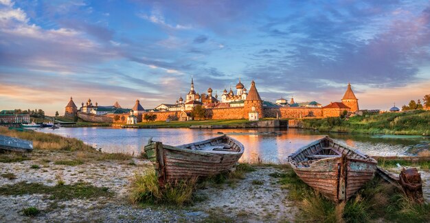 Vecchie barche di legno sulla riva della baia della prosperità sull'isola di Solovetsky e una vista dei templi del monastero di Solovetsky sotto i raggi del sole al tramonto