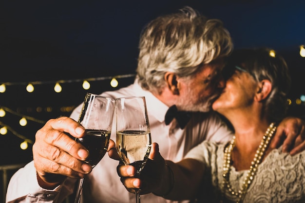 Vecchie coppie caucasiche che si baciano mentre brindano a bicchieri di champagne per celebrare la festa di Capodanno Marito e moglie amorevoli che si baciano mentre fanno festa con bicchieri di vino bianco in mano