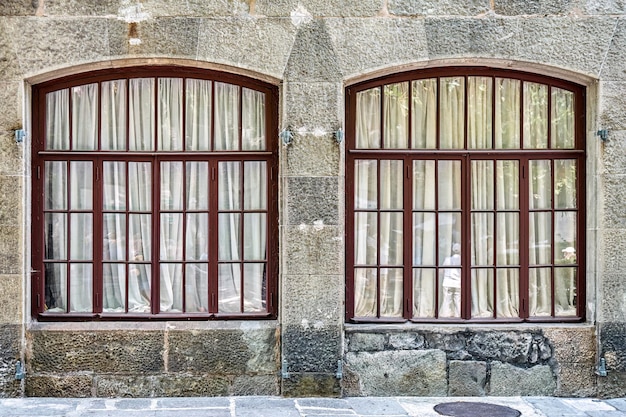 Vecchie finestre ad arco con tende bianche sullo storico muro di pietra