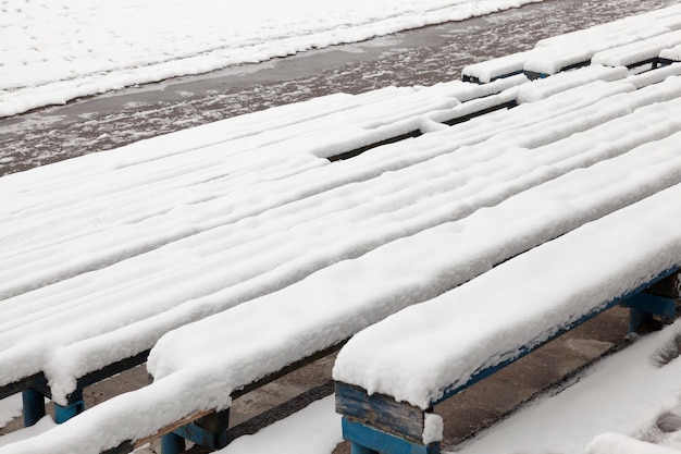 Vecchie panche di legno nello stadio, coperte di neve nella stagione invernale