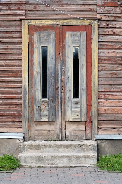 Vecchie porte di legno rosso ingresso alla casa di legno con vernice sbucciata appassita sulle pareti a Tartu Estonia