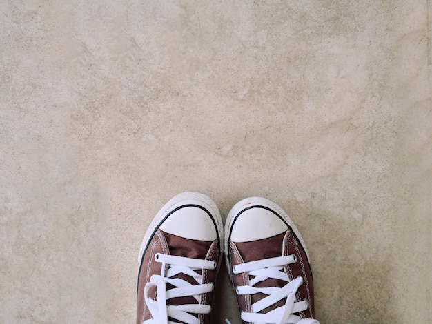 Vecchie scarpe da ginnastica marroni, poste su uno sfondo di cemento.