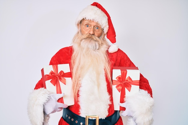 Vecchio anziano che indossa il costume di Babbo Natale che tiene in mano i regali espressione ignara e confusa concetto di dubbio