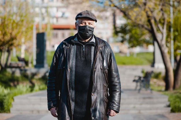 Vecchio armeno con cappello nero che indossa maschera medica in strada in primavera e guardando davanti