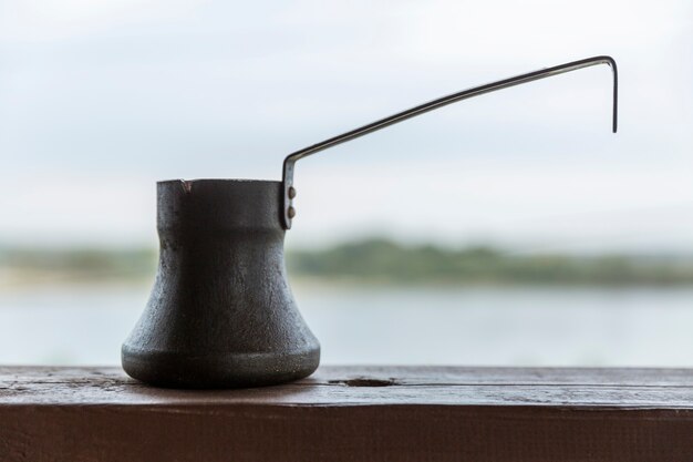 Vecchio cezve per il caffè su un davanzale in legno con una bellissima vista. Avvicinamento. Un ottimo inizio di giornata.