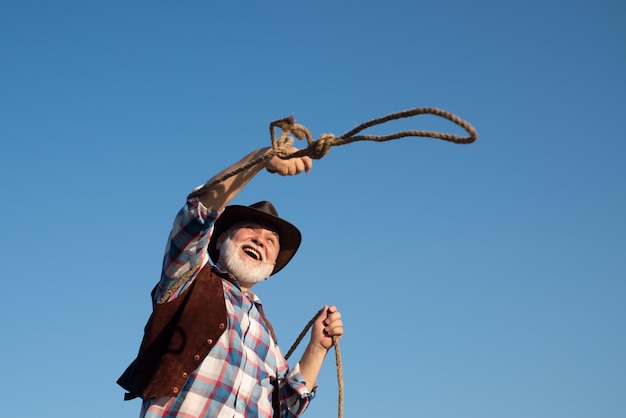 Vecchio cowboy occidentale con la corda del lazo. Uomo barbuto del selvaggio west con giacca marrone e cappello.