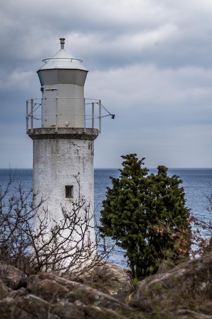 Vecchio faro bianco sulla costa rocciosa contro un cielo nuvoloso
