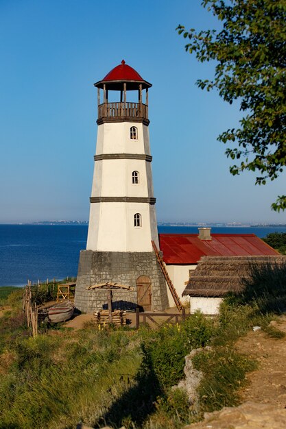 Vecchio faro con un tetto rosso in riva al mare al mattino.