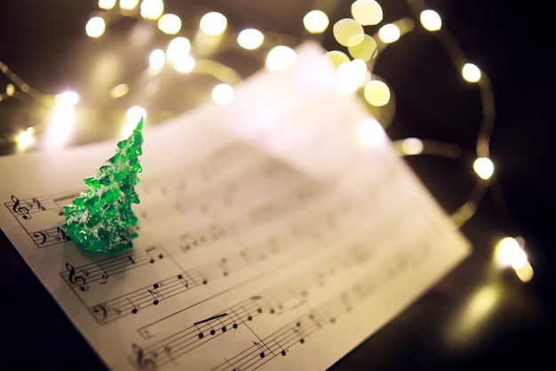 Vecchio foglio con note musicali di Natale come sfondo contro luci sfocate. Concetto di musica di Natale