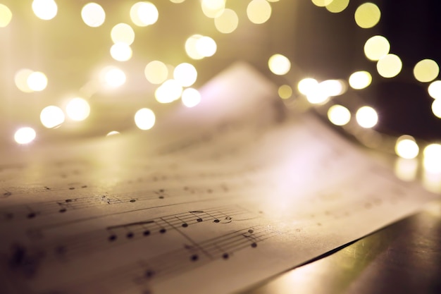 Vecchio foglio con note musicali di Natale come sfondo contro luci sfocate. Concetto di musica di Natale