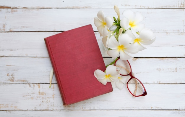 vecchio libro rosso, occhiali e fiori bianchi su fondo di legno, vintage