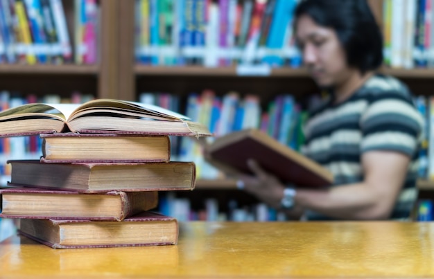 Vecchio libro sullo scrittorio in biblioteca con l&#39;uomo che legge la priorità bassa del libro