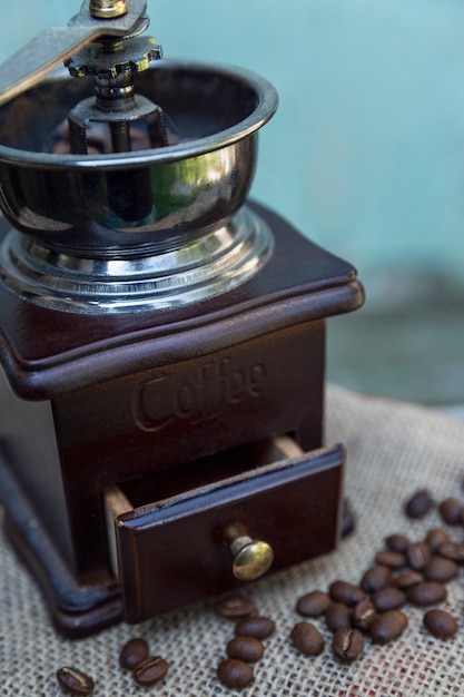 Vecchio macinino da caffè su uno sfondo di legno azzurro con chicchi di caffè sparsi. Verticale.