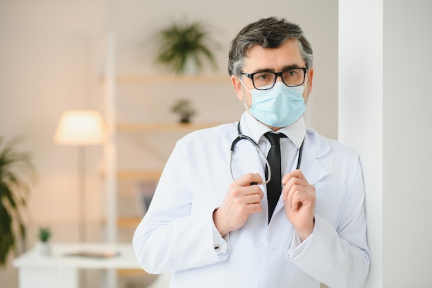 Vecchio medico professionista sanitario maturo che indossa occhiali stetoscopio a camice bianco e maschera facciale Concetto di protezione sanitaria del personale medico Ritratto