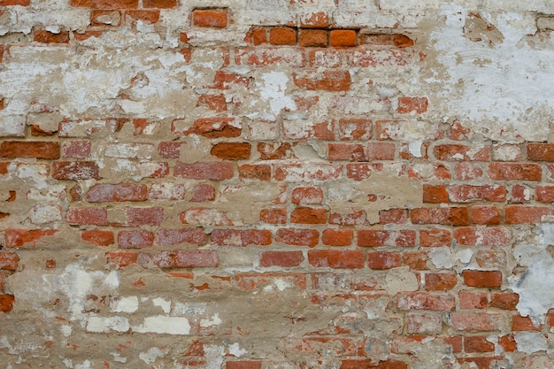 Vecchio muro di mattoni stagionato rosso con pezzi battuti di calce, mastice e sfondo di gesso