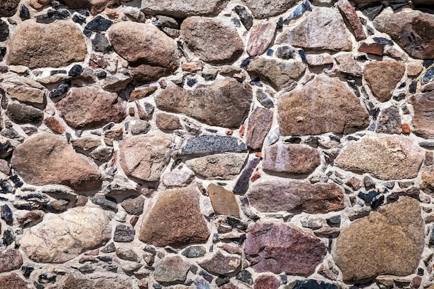 Vecchio muro fatto di grosse pietre e mattoni rotti. Fondo grezzo d'annata della superficie dei blocchi