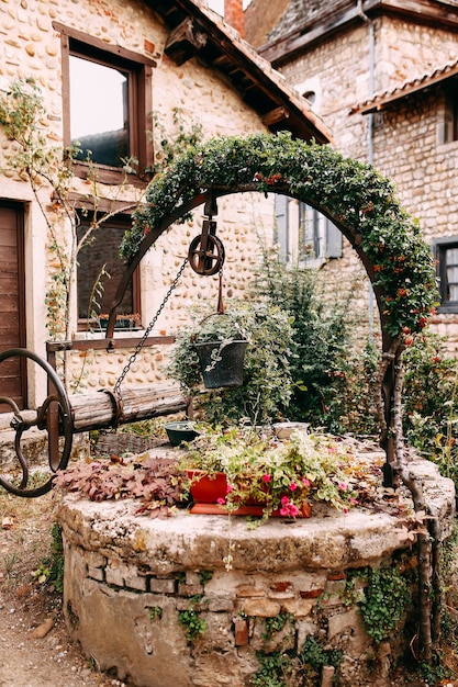 Vecchio pozzo di pietra in legno con arco di fiori rossi ed edera a Perouges, Francia. Foto di alta qualità