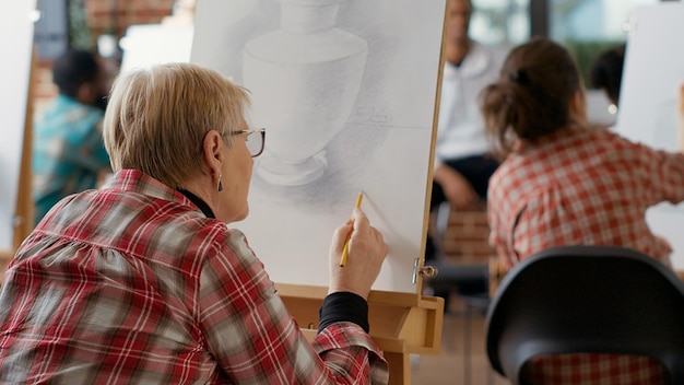 Vecchio studente che usa la matita per disegnare il modello di ispirazione a lezione, crea uno schizzo di opere d'arte professionali, frequenta un programma artistico per sviluppare abilità di disegno su tela. Crescita personale. Colpo a mano libera