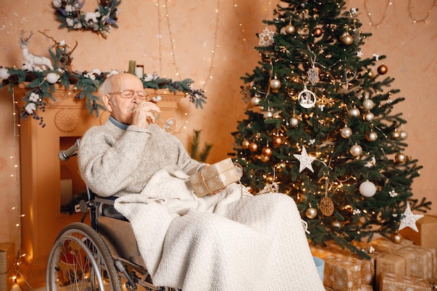 Vecchio su una sedia a rotelle seduto vicino all'albero di Natale e con in mano una confezione regalo