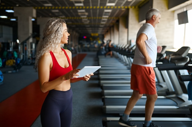 Vecchio sul tapis roulant, trainer femminile con laptop