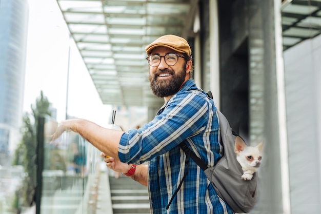 Vedere moglie. Uomo barbuto con gli occhiali e il cappello che sorride mentre vede sua moglie venire da lui