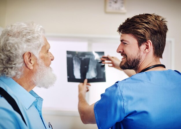 Vedete, non c'è niente di cui preoccuparsi Inquadratura di un giovane dottore e del suo paziente anziano che guardano insieme una radiografia