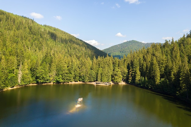 Veduta aerea del grande lago con acque cristalline tra le colline di alta montagna ricoperte da una fitta foresta sempreverde.