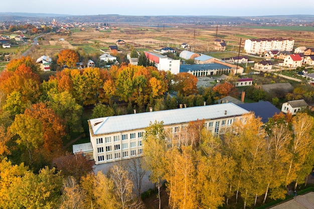 Veduta aerea dell'edificio scolastico o dell'asilo con un grande cortile tra gli alberi autunnali sullo sfondo del paesaggio rurale