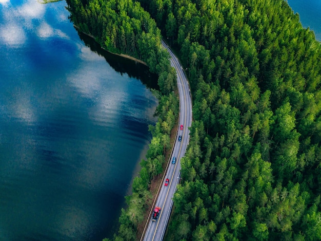 Veduta aerea della strada con le automobili tra la foresta verde e l'acqua blu del lago in estate Finlandia