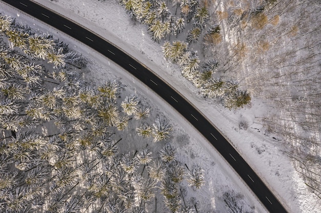 Veduta aerea della strada invernale nella foresta innevata. Colpo catturato dal drone dall'alto