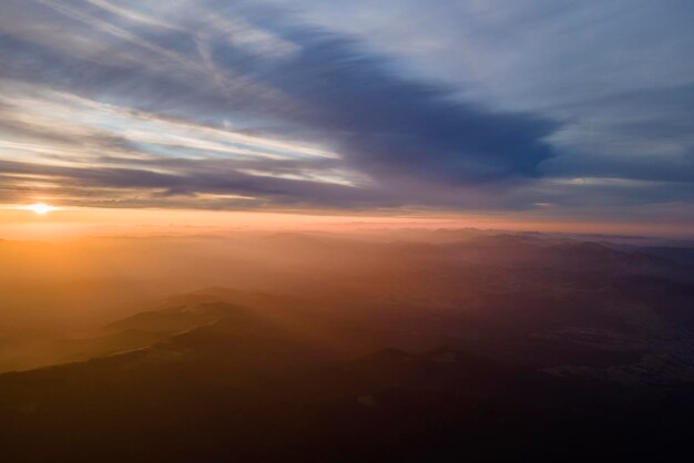 Veduta aerea delle scure colline di montagna con i raggi luminosi del sole al tramonto Vette nebbiose e valli nebbiose la sera
