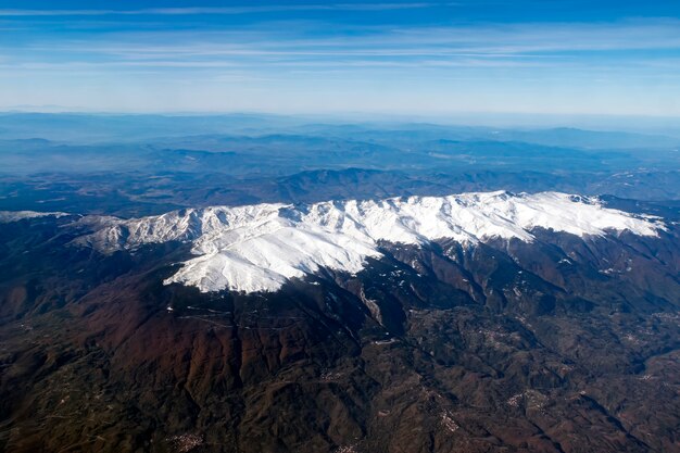 Veduta aerea di una valle con cime montane bianche, linea dell'orizzonte nebbiosa e skyscape. Vista panoramica dalla finestra di un volo che passa sulle montagne. Creste di neve e colline in una valle. Volo sopra le montagne