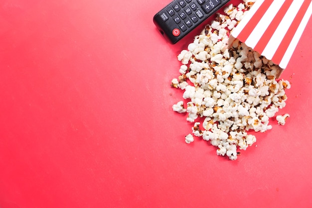 Veduta dall'alto di popcorn e telecomando della TV su sfondo rosso.