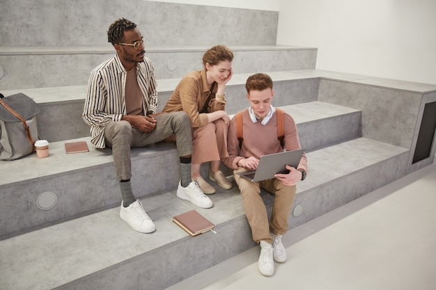 Veduta dall'alto di un gruppo di studenti che usano il laptop insieme e chiacchierano nella moderna lounge del college, copia spazio