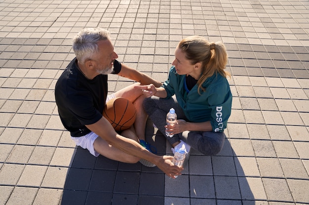 Veduta dall'alto di una coppia matura in abbigliamento sportivo che conversa mentre si beve acqua rilassante