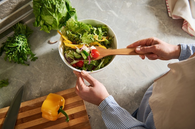 Veduta dall'alto di una donna che mescola insalata con un cucchiaio di legno nel tavolo della cucina.