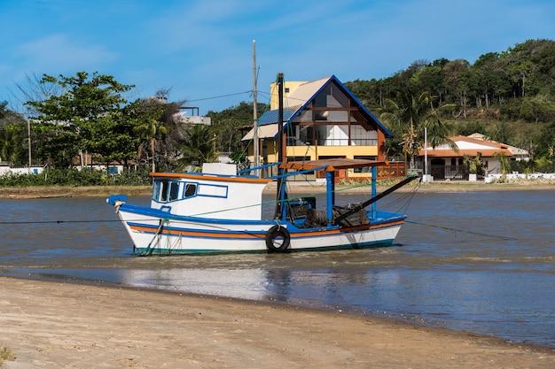 Veduta della spiaggia di Rio das Ostras con la riunione del fiume a Rio de Janeiro. Giornata di sole, cielo blu. Sabbia gialla e alcune rocce. Ponte in legno da attraversare. Barche e pesca sul molo.