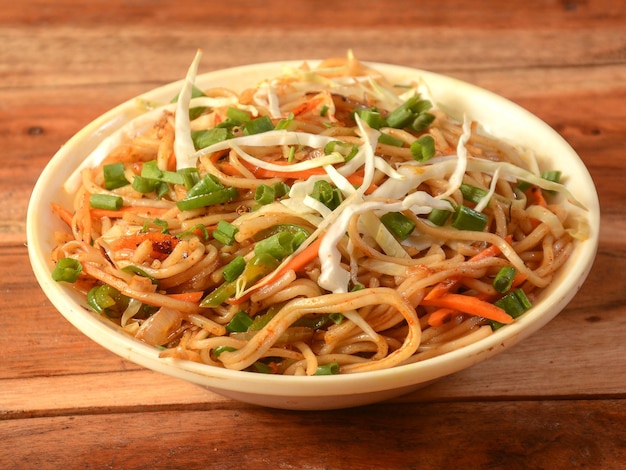 Veg Hakka Noodles un popolare piatto orientale a base di noodles e verdure servito su uno sfondo di legno rustico con fuoco selettivo