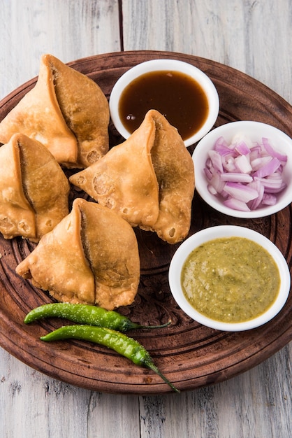 Veg Samosa - è uno snack indiano croccante e speziato a forma di triangolo per l'ora del tè servito con peperoncino verde fritto, cipolla e chutney o ketchup