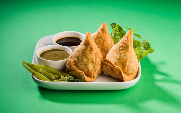 Veg Samosa è uno snack popolare indiano o cibo spazzatura servito con peperoncino verde fritto, cipolla e chutney o ketchup