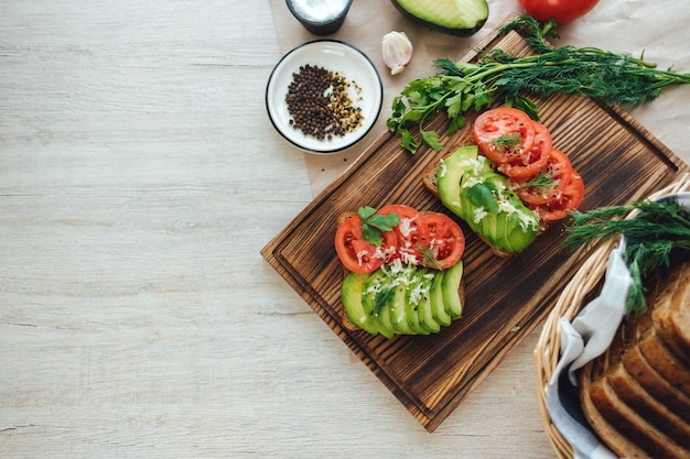 Vegano sano panino fatto in casa, avocado e pomodori con pane di grano scuro su una tavola di legno.