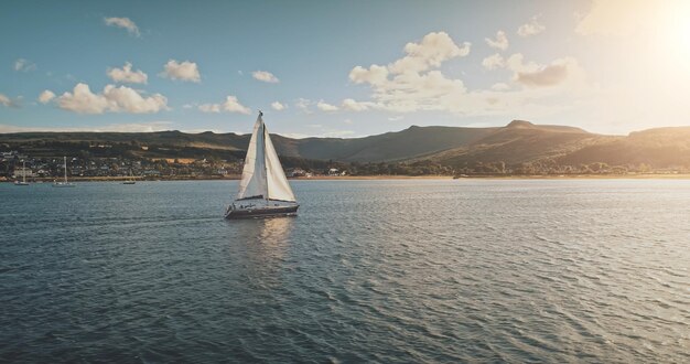 Vela su uno yacht da corsa in mare aperto, sole, splendore, vista aerea, maestoso paesaggio marino sulla costa dell'isola di Arran