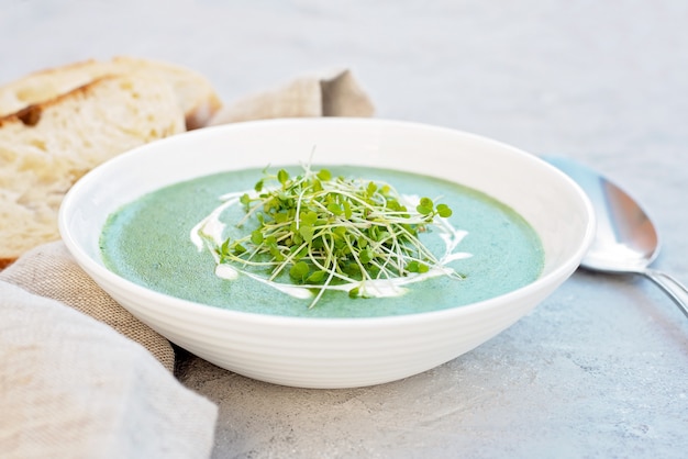 Vellutata di spinaci freschi con rucola microgreen in un piatto bianco con pane ciabatta